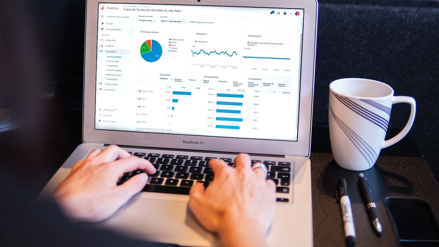 Hands typing on a laptop showing a dashboard, beside a cup of coffee
